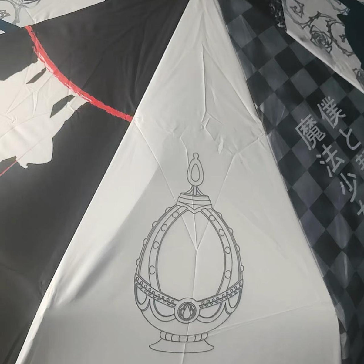 Close-up of the Madoka Magica umbrella canopy — off-white panel with the Witch stay night crest line art beside a black panel with red trim