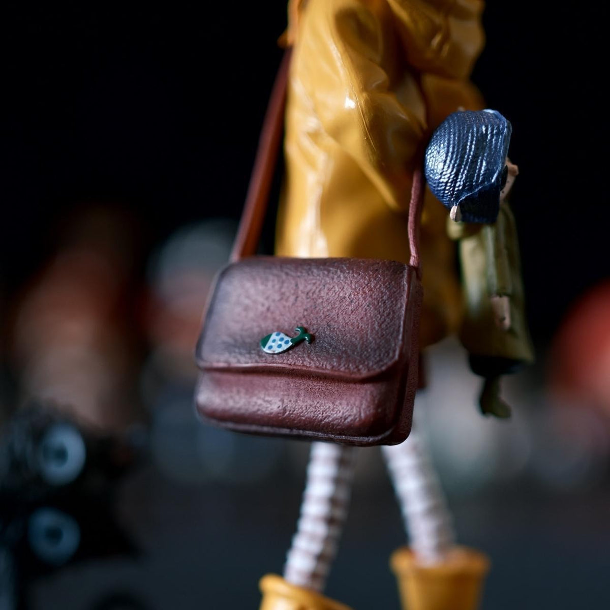 Close-up of the Coraline figure's brown crossbody satchel with a small green leaf charm on the flap